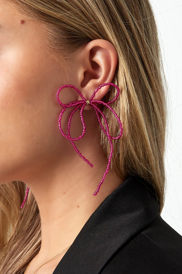 model draagt stainless steel oorbellen met strik en roze kralen Mara Jewellery